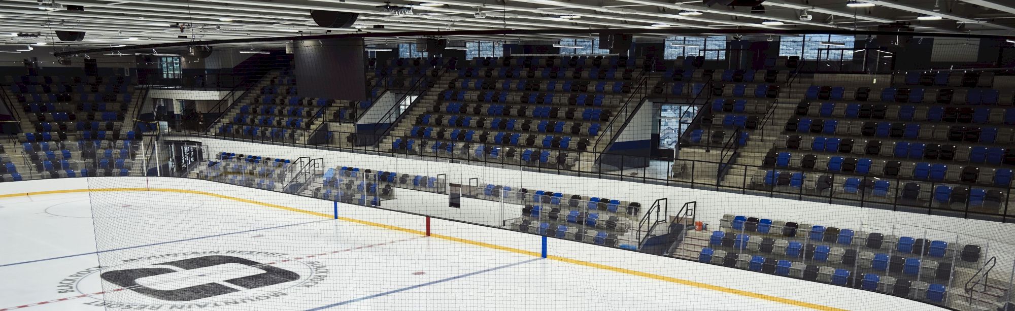 An empty indoor ice hockey rink with protective glass, boards, markings, and seating stands surrounding the ice, quiet and ready for games.