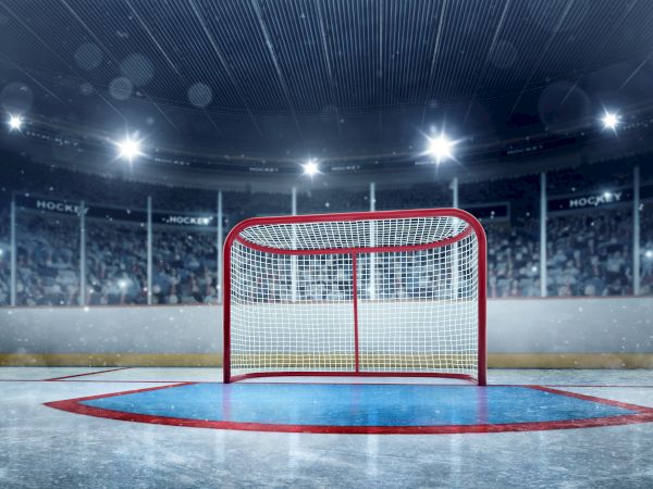 A red hockey goal on an ice rink inside a lit arena, empty stands in the background, cool blue tones, subtle reflections, end sentence at 140 chars.