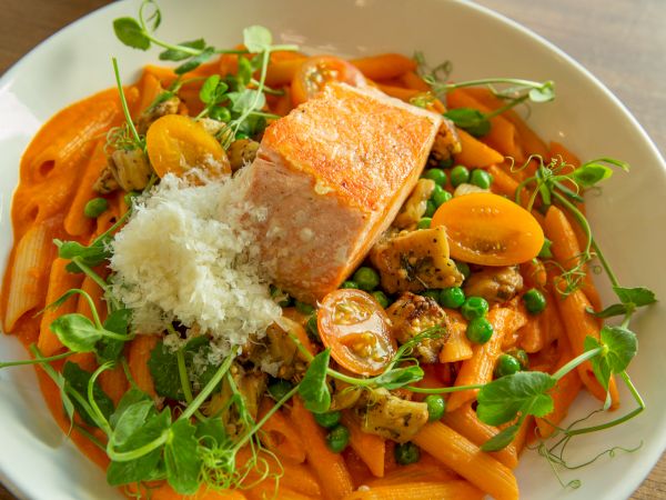 Creamy orange pasta with peas, mushrooms, and crumbled cheese topped by crispy salmon; fresh greens add color and texture.