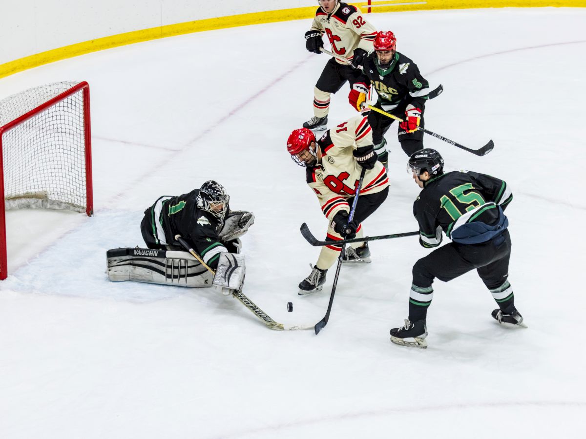 Ice hockey action: a goalie sprawls near the net as players scramble for the puck in a tense scoring chance.