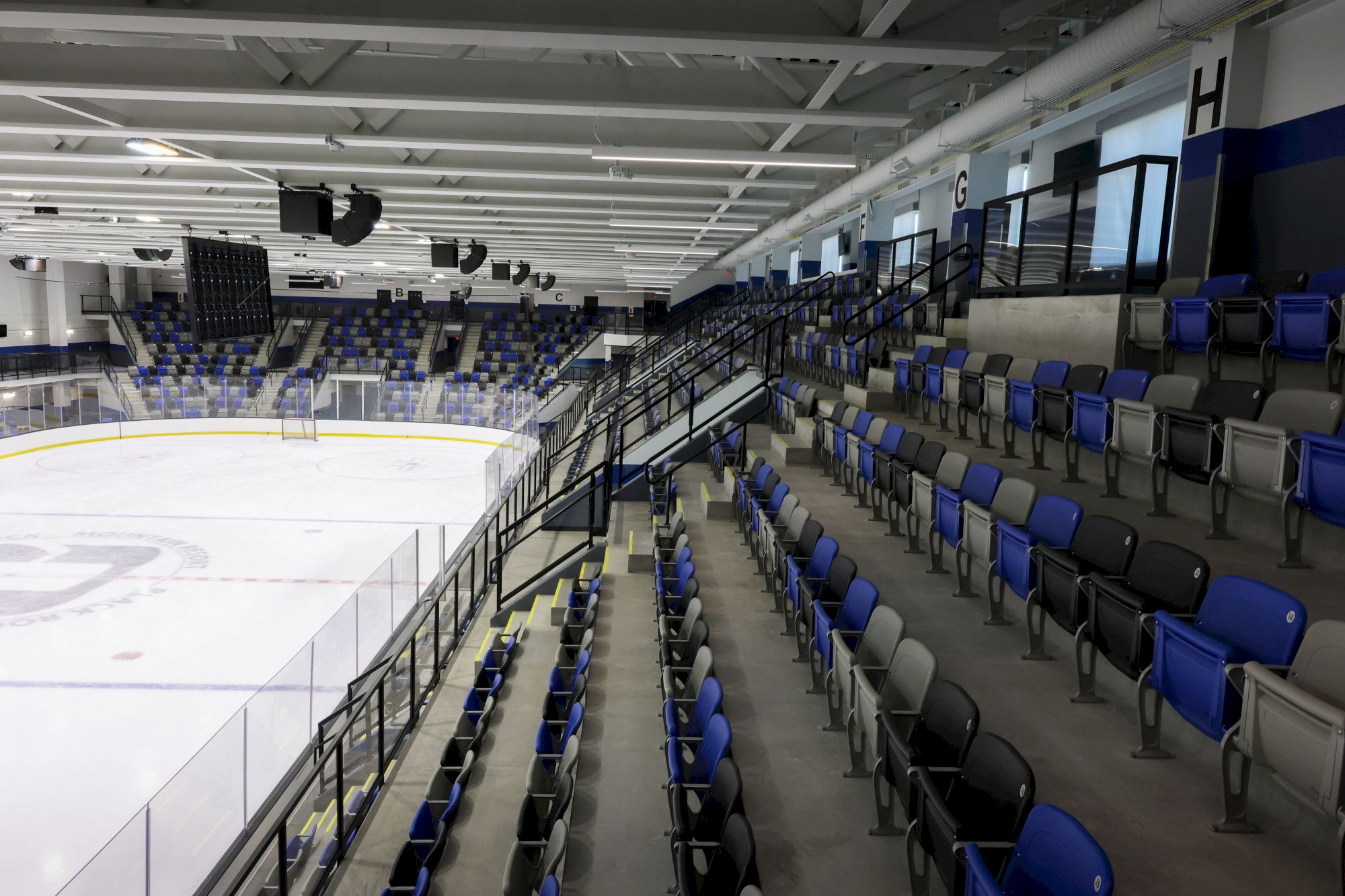 An empty indoor ice hockey rink with blue and black seats arranged in rows along the low, curved stands.