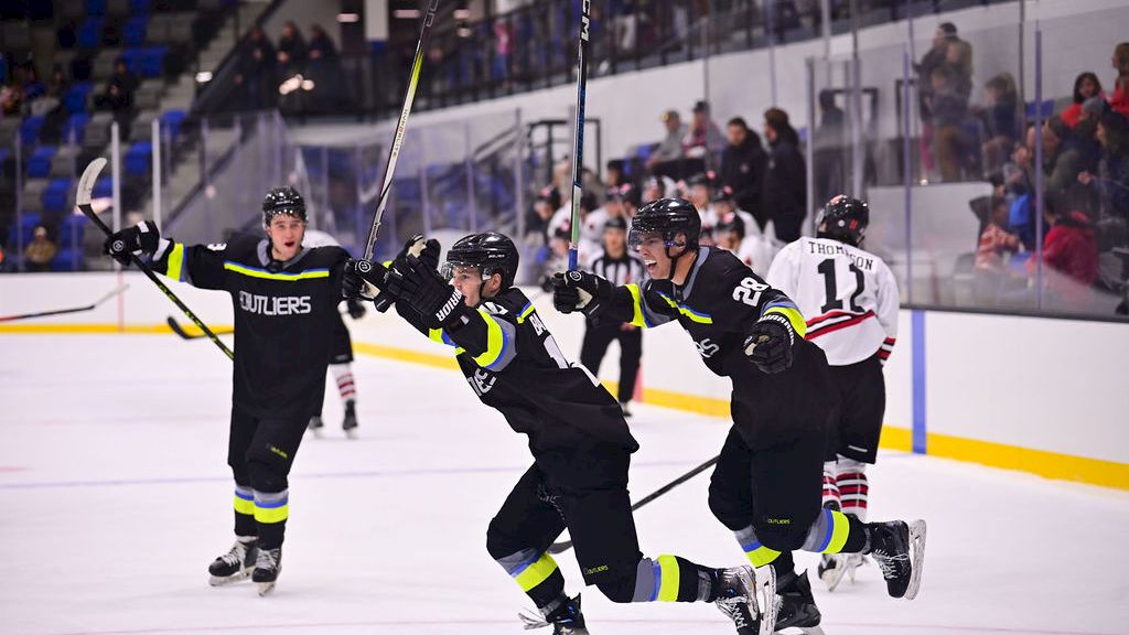 A group of hockey players in black uniforms celebrate on the ice as teammates skate with arms raised in triumph.